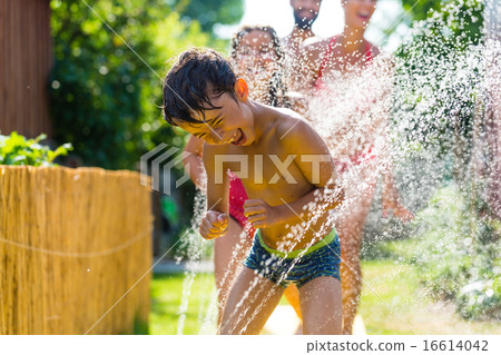 Family cooling down with sprinkler in garden Family cooling down with sprinkler in garden 16614042