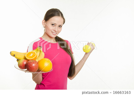 Girl athlete holding a plate of fruit and dumbbell 16663163