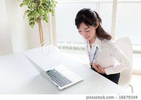 A young woman holding a stomach with a stomach ache in front of a personal computer at the office window 16679394