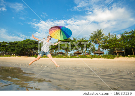 Cheerful young girl with rainbow umbrella having fun on the beach before sunset. Travel, holidays Cheerful young girl with rainbow umbrella having fun on the beach before sunset. Travel, holidays 16683129