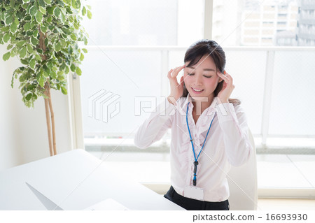 A young woman who holds the temple with headaches in front of a personal computer at the office window window OL 16693930