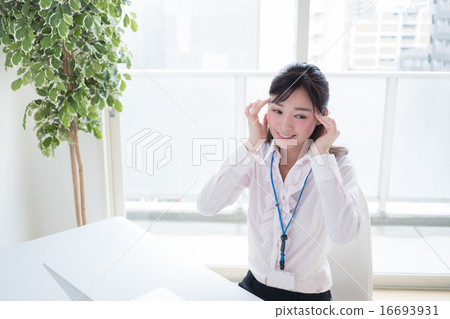 A young woman who holds the temple with headaches in front of a personal computer at the office window window OL 16693931