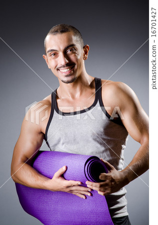 Muscular man with mat in studio 16701427