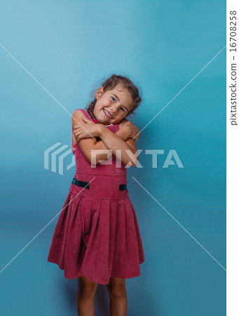 Girl European appearance decade hugging herself on a blue backgr Girl European appearance decade hugging herself on a blue backgr 16708258