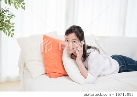 A young lady who is lying on the sofa and calling on a smartphone A young lady who is lying on the sofa and calling on a smartphone 16713095