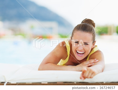 Smiling young woman laying on chaise-longue and pointing in came 16724657