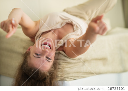Laughing young woman laying on couch and pointing in camera 16725101