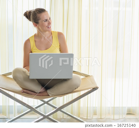 Smiling young woman on modern chair with laptop looking on copy Smiling young woman on modern chair with laptop looking on copy 16725140