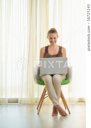 Happy young woman sitting on modern chair and using laptop Happy young woman sitting on modern chair and using laptop 16725143