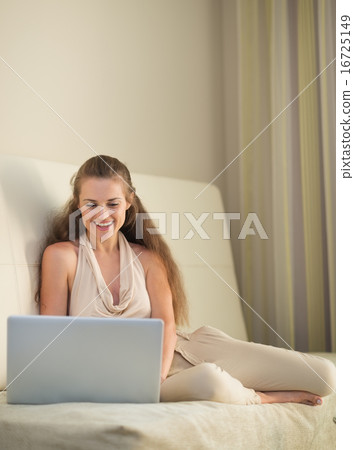 Smiling young woman on couch with laptop Smiling young woman on couch with laptop 16725149