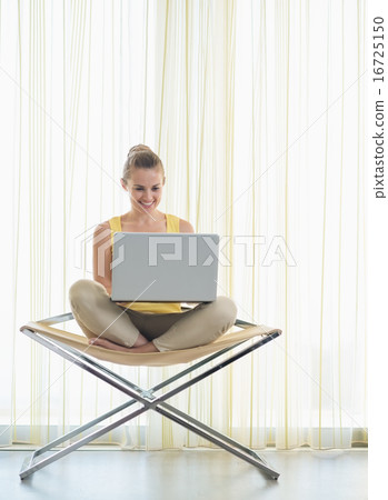 Happy young woman sitting on modern chair with laptop Happy young woman sitting on modern chair with laptop 16725150