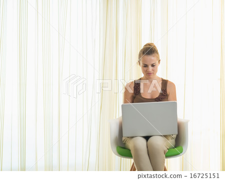 Young woman sitting on modern chair and using laptop Young woman sitting on modern chair and using laptop 16725151