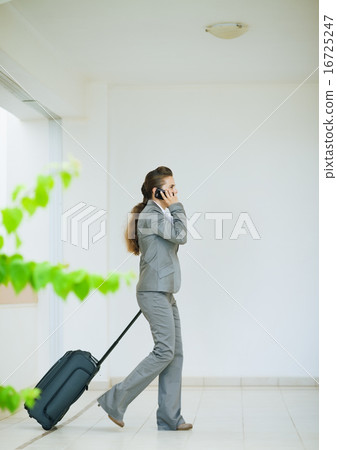 Business woman in business trip with wheel bag speaking mobile Business woman in business trip with wheel bag speaking mobile 16725247
