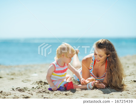 Mother and baby girl playing with sand on beach Mother and baby girl playing with sand on beach 16725439