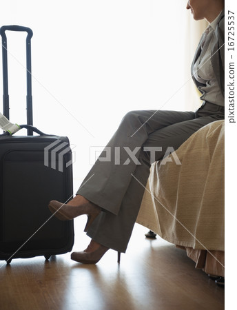 Tired business woman sitting on bed in hotel room after trip 16725537