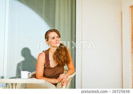 Thoughtful young female sitting on terrace with cup of tea and 16725636