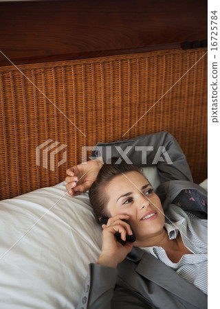 Business woman laying on bed in hotel room and talking cell phon Business woman laying on bed in hotel room and talking cell phon 16725784