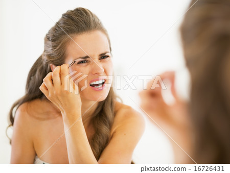 Displeased young woman tweezing eyebrows 16726431