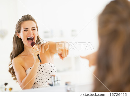 Happy young woman singing in makeup brush in bathroom 16726433