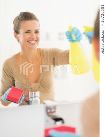 Smiling young housewife cleaning mirror in bathroom Smiling young housewife cleaning mirror in bathroom 16726581