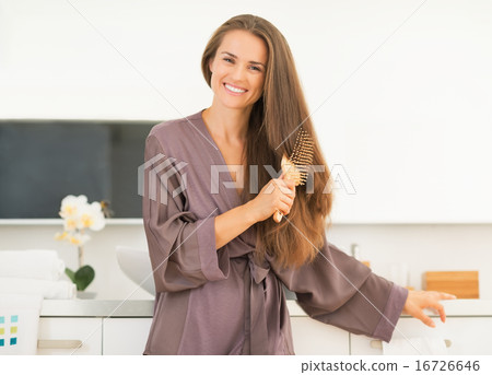 Happy young woman combing hair in bathroom 16726646