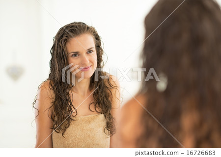 Portrait of young woman with wet hair looking in mirror Portrait of young woman with wet hair looking in mirror 16726683