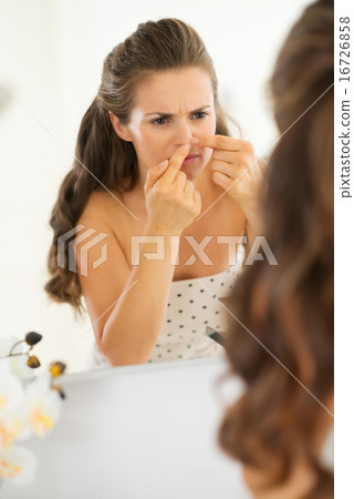 Young woman squeezing acne in bathroom 16726858