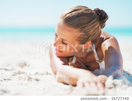 Relaxed young woman in swimsuit laying on sandy beach 16727340