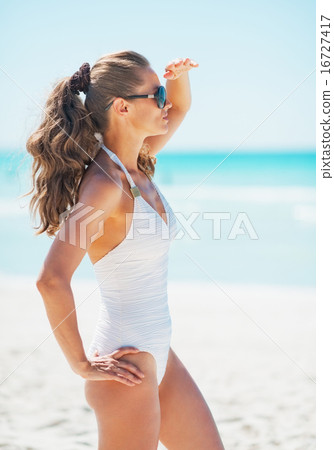 Young woman in swimsuit and sunglasses on beach looking into dis 16727417