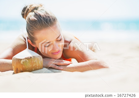 Relaxed young woman laying on beach with coconut 16727426