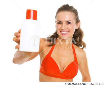 Smiling young woman in swimsuit giving bottle of sun block creme Smiling young woman in swimsuit giving bottle of sun block creme 16728439