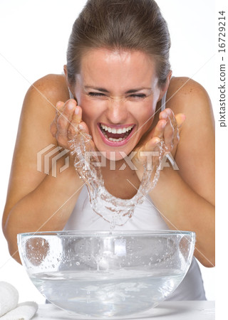 Happy young woman washing face in glass bowl with water 16729214