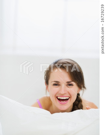 Smiling girl laying in bed and hiding behind pillow Smiling girl laying in bed and hiding behind pillow 16729239