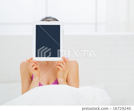 Woman sitting in bed and hiding tablet PC in front of face Woman sitting in bed and hiding tablet PC in front of face 16729240