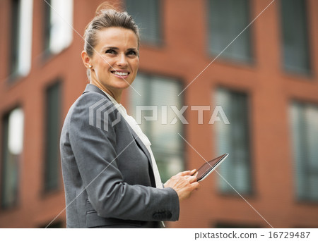 Smiling business woman with tablet pc in front of office buildin 16729487