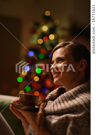 Thoughtful woman sitting chair and drinking hot beverage in fron 16731621