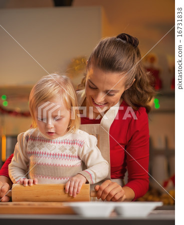 Mother and baby rolling pin dough in christmas decorated kitchen 16731838