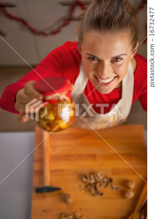 Portrait of happy young housewife showing jar with honey nuts Portrait of happy young housewife showing jar with honey nuts 16732477