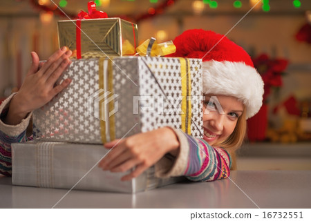 Smiling teenage girl in santa hat looking out from stack of chri 16732551