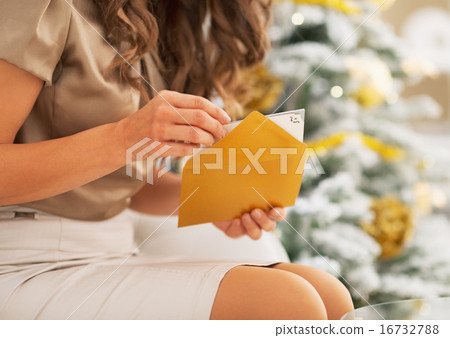 Closeup on woman opening christmas postcard near christmas tree 16732788