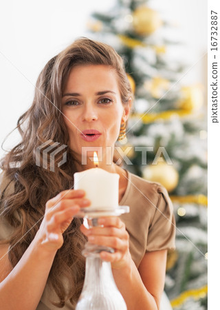 Young woman blowing candle in front of christmas tree Young woman blowing candle in front of christmas tree 16732887