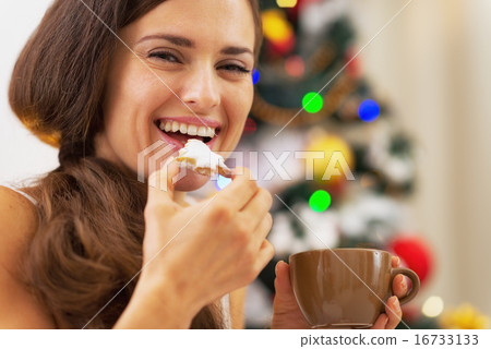 Happy young woman in pajamas having snack near christmas tree Happy young woman in pajamas having snack near christmas tree 16733133