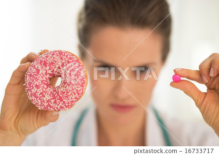 Closeup on serious medical doctor woman showing donut and pill Closeup on serious medical doctor woman showing donut and pill 16733717