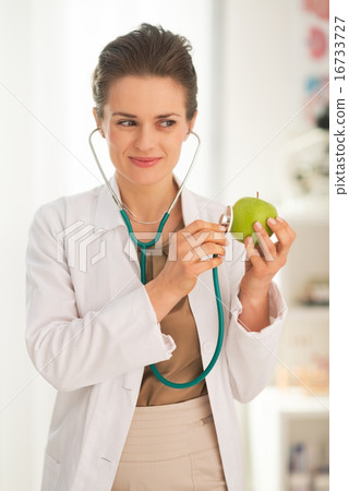 Happy medical doctor woman examining apple with stethoscope Happy medical doctor woman examining apple with stethoscope 16733727