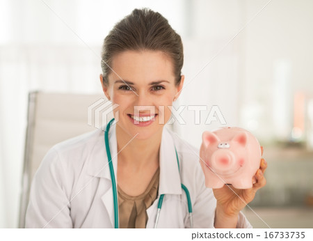 Portrait of happy doctor woman showing piggy bank Portrait of happy doctor woman showing piggy bank 16733735