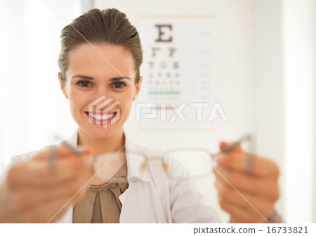 Smiling ophthalmologist doctor woman giving eyeglasses in front Smiling ophthalmologist doctor woman giving eyeglasses in front 16733821