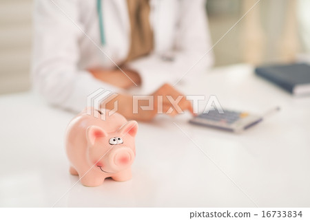 Closeup on piggy bank and medical doctor woman using calculator 16733834