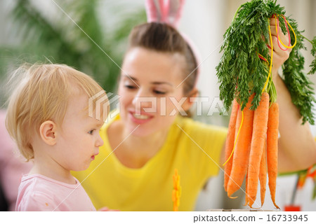 Mother showing baby bunch of carrots 16733945