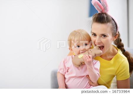 Mother and baby biting chocolate Easter rabbit cookie 16733964