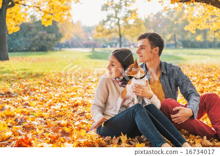 Young couple sitting outdoors in autumn park with dog and lookin Young couple sitting outdoors in autumn park with dog and lookin 16734017